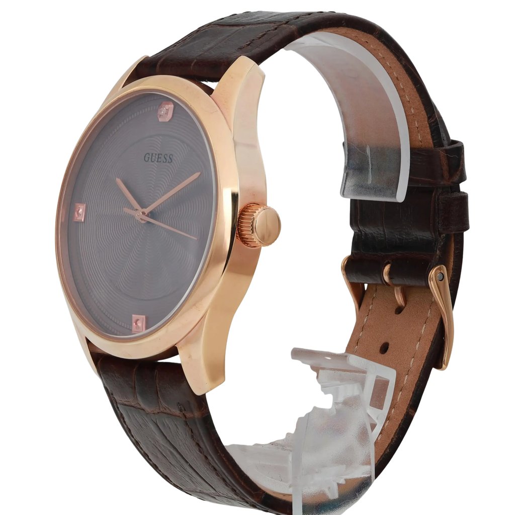 An image of a pre-owned men's GUESS wristwatch, positioned at a slight angle, showcasing the side and partial front view. The watch features a rose gold-tone case and a textured dark brown leather strap. The dial is dark with minimalist hour markers. The image is taken at a close distance to highlight the details and craftsmanship of the watch.