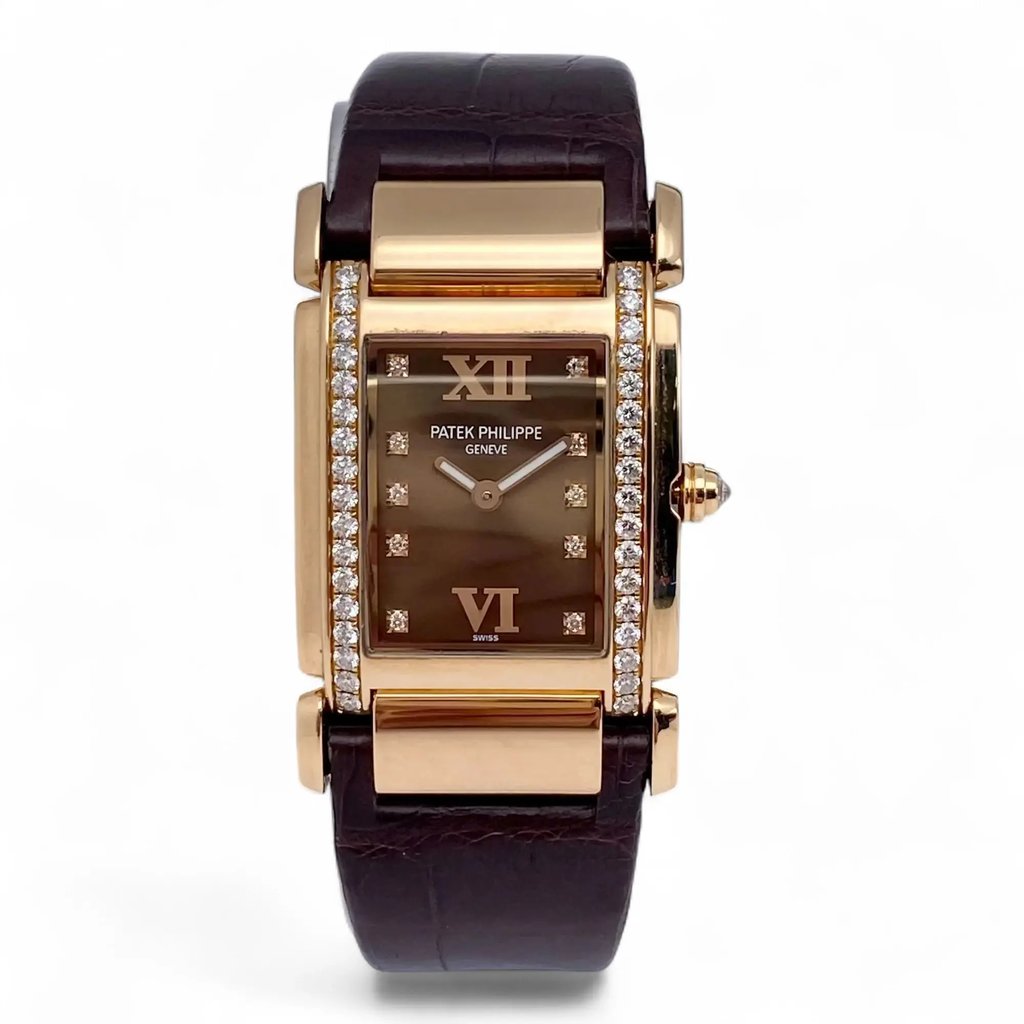 An image of a pre-owned women's Patek Philippe twenty-4 18K Rose Gold Diamond Chocolate Dial Ladies Watch 4920R wristwatch captured from a front-facing angle. The watch features a rectangular face with a chocolate dial, Roman numerals at the 12 and 6 positions, and diamond hour markers. The case is bordered with a double row of sparkling diamonds, and the watch is fitted with a dark leather strap. The image is taken at a close distance, highlighting the luxurious details and craftsmanship.