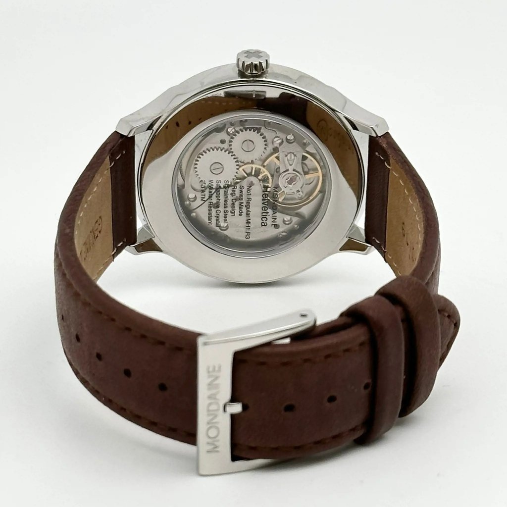 An image of a Wristwatch by Mondaine. This Display Model item is designed for Men, featuring a Casual style. It has a Mechanical (Manual) movement and an Analog display with a Silver dial color. The indices include 12-Hour Dial,Arabic Numerals. The band is made of Leather and the case is made of Stainless Steel. The watch has a Round shape with a case size of 41 mm and a case thickness of 10 mm.