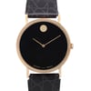 An image of a pre-owned wristwatch taken from a front close-up angle, showcasing the watch face prominently. The watch features a sleek black dial with a minimalistic design, including two gold hands and a gold dot at the 12 o'clock position. The casing is gold-toned, complementing the black leather strap with a textured pattern. The brand names "Movado" and "Zenith" are subtly visible at the bottom of the dial.