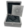 An image of an empty wristwatch box viewed from a slight overhead angle. The box is open, revealing a soft, black interior with a booklet resting inside. The booklet features an intricate geometric design on its cover. The box is positioned centrally in the frame, and the image is taken from a close distance to capture the details of the box's texture and design.