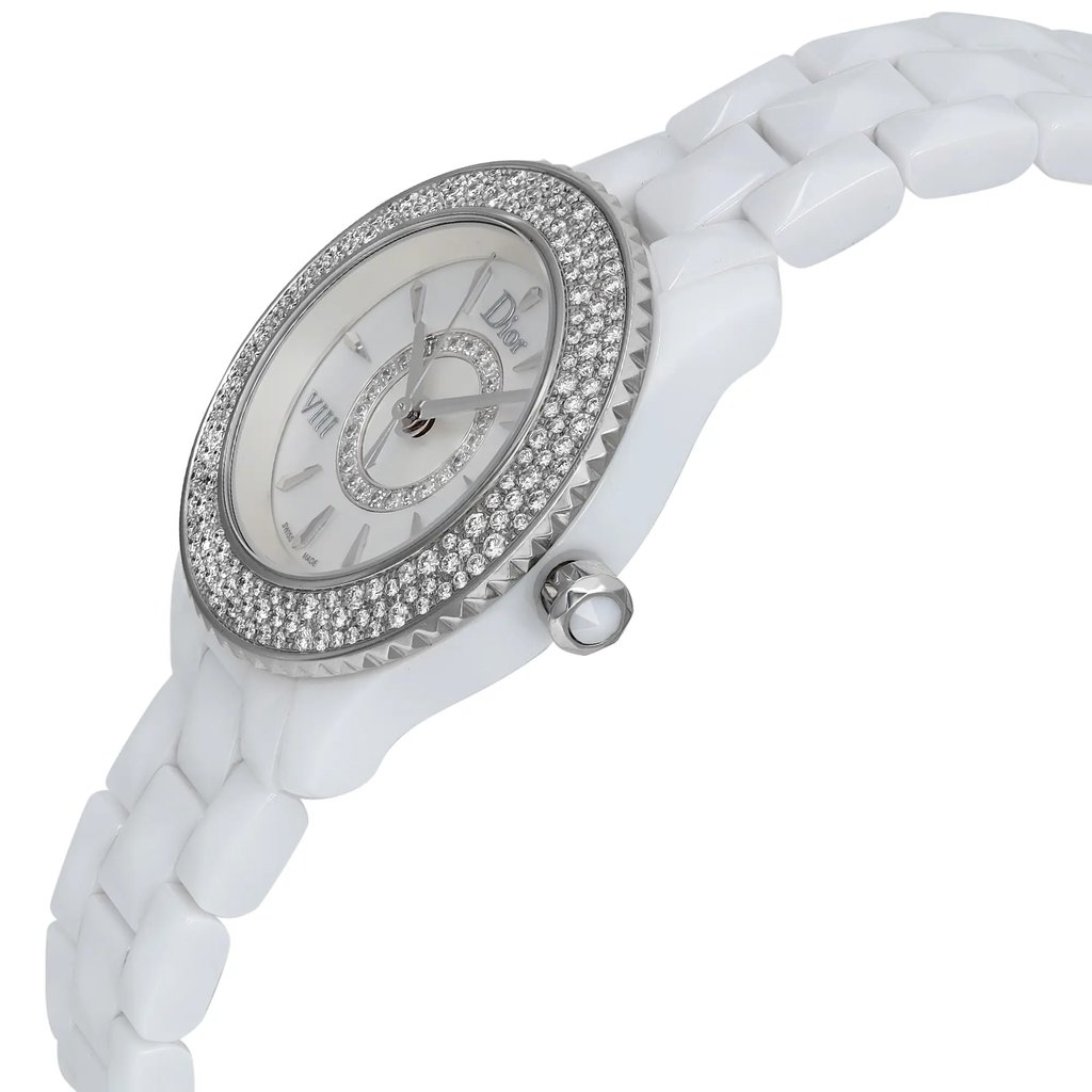 An image of a pre-owned wristwatch captured from a side profile view, showcasing the watch's crown prominently. The angle highlights the intricate detailing on the bezel, which is adorned with small gemstones. The watch face features Roman numerals and elegant hands, while the bracelet is composed of smooth, white links. The photograph is taken at a close distance, emphasizing the luxurious design elements.