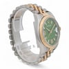 An image of a pre-owned Rolex unisex adult wristwatch, taken from a slightly elevated angle showing the right side. The watch features a two-tone metal bracelet and a green dial with a date indicator and luminous hands. The watch is positioned at a close distance, highlighting its detailed craftsmanship and design elements.