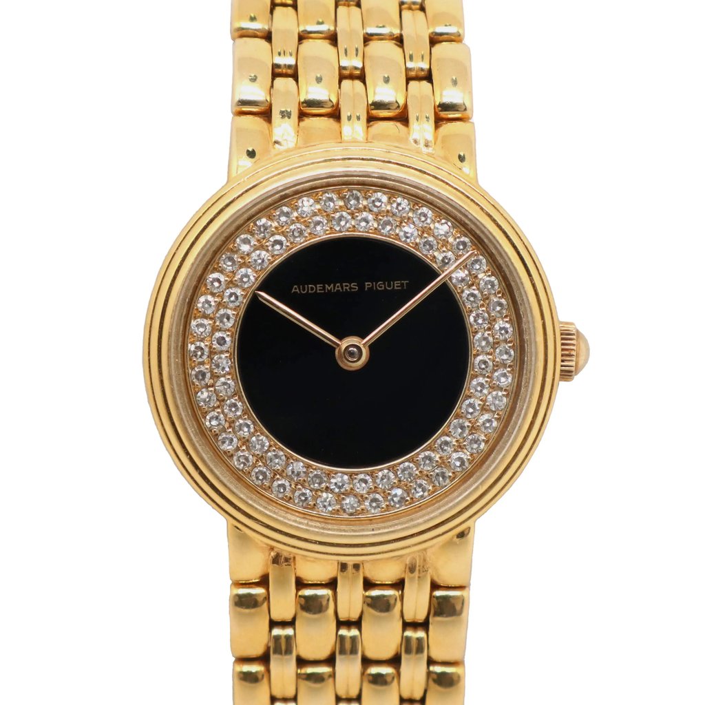 An image of a pre-owned women's Audemars Piguet wristwatch. The watch is positioned upright, showcasing a frontal view. It features a gold bracelet and a round, onyx dial surrounded by a ring of sparkling diamonds. The brand name is visible on the dial, and the watch is photographed from a close distance, capturing intricate details and angles.