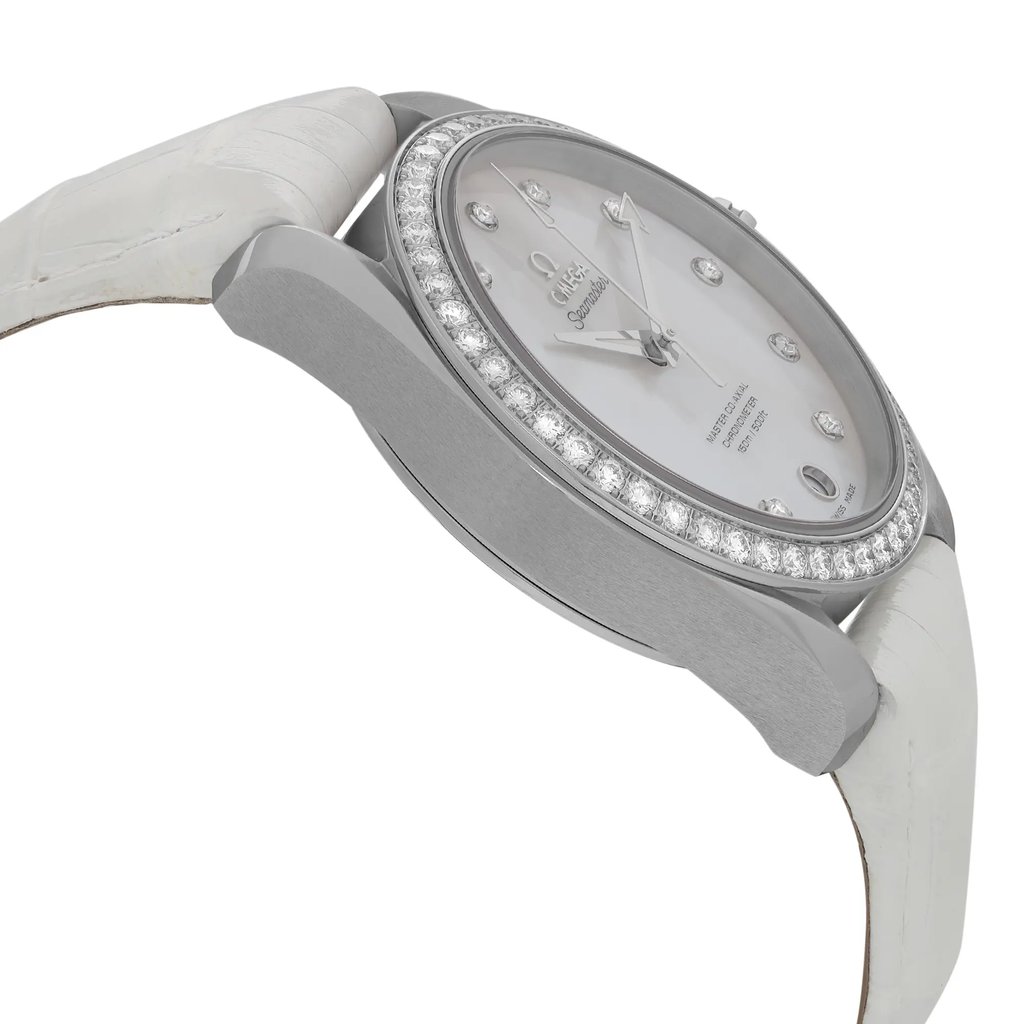 An image of a women's OMEGA wristwatch, photographed from a slightly angled side perspective, focusing on the left side of the case. The watch features a steel factory bezel adorned with small diamonds, a mother of pearl factory dial with luminous hands, and a date indicator. The strap is white and the image is taken in close-up to highlight the details of the watch's design.