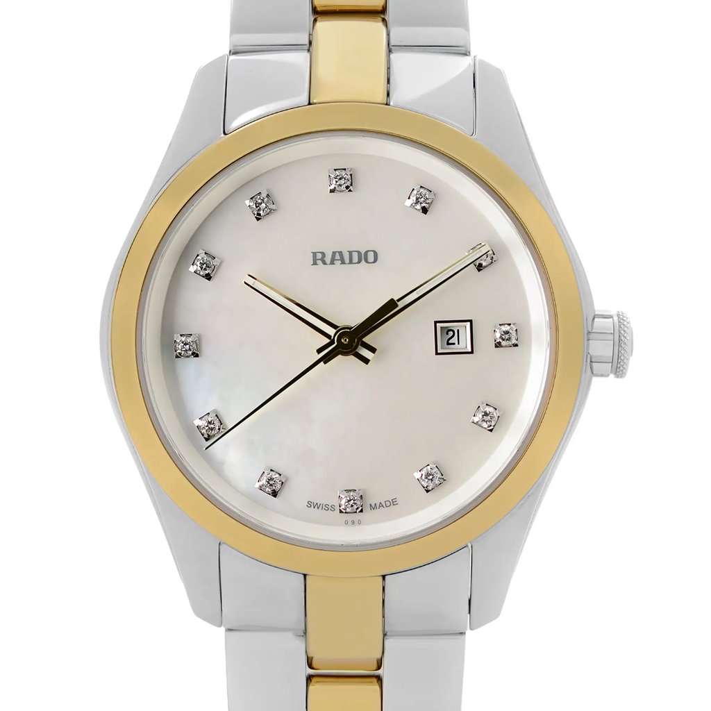 An image of a wristwatch taken from the front in a close-up shot, focusing on the watch face. The watch features a gold and silver-toned case and bracelet. The dial is adorned with diamond-like hour markers and has a date display at the 3 o'clock position. The brand name is visible just below the 12 o'clock marker.