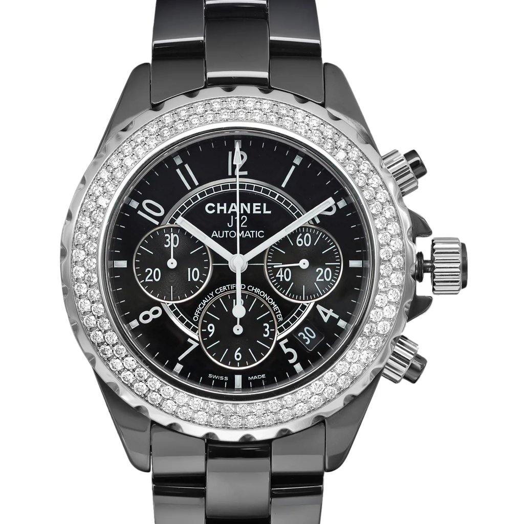 An image of a pre-owned wristwatch shown in a front close-up shot. The watch face features a black dial with silver markings and three sub-dials. It has a polished metal bezel embellished with sparkling stones. The watch's crown and pushers are visible on the right side, and the metal bracelet is partially shown.