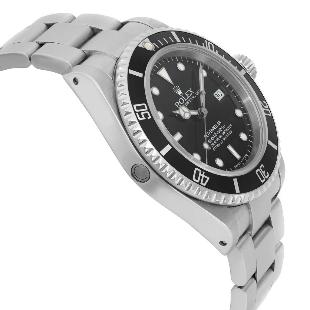 An image of a pre-owned men's Rolex diver wristwatch, viewed from a side profile opposite the crown. The watch features a round shape with a black dial and black bezel. It has a stainless steel case and band, with visible links. The watch includes a date indicator and luminous hands. The angle captures the watch at a close distance, highlighting its sleek design and material.
