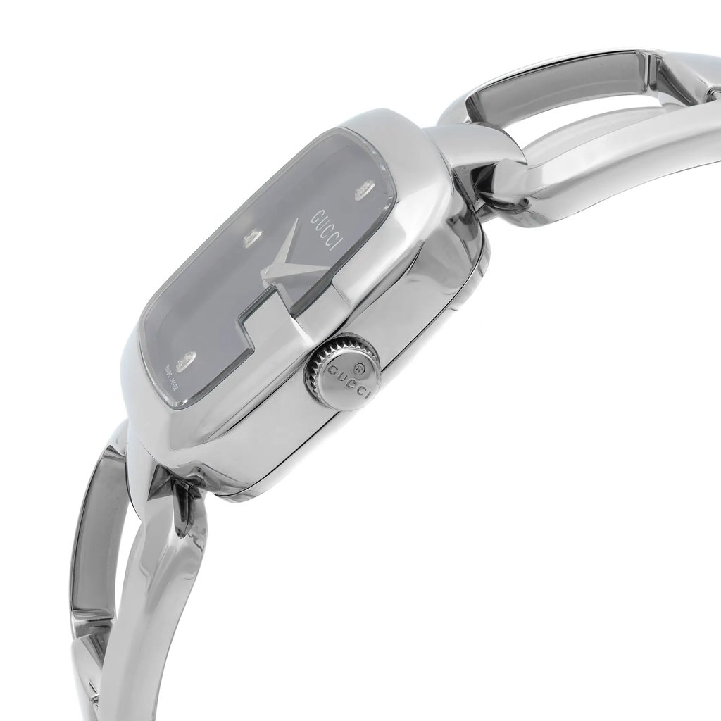 An image of a pre-owned Gucci wristwatch for women, showcasing a side profile view with the crown visible. The watch has a dress/formal style, featuring a black sunburst pattern dial, housed within a round stainless steel case. The bezel is silver in color, complementing the stainless steel band. The angle of the photo gives a clear view of the watch's side, including the curvature of the links on the band, and is taken from a close distance to highlight the watch's details.