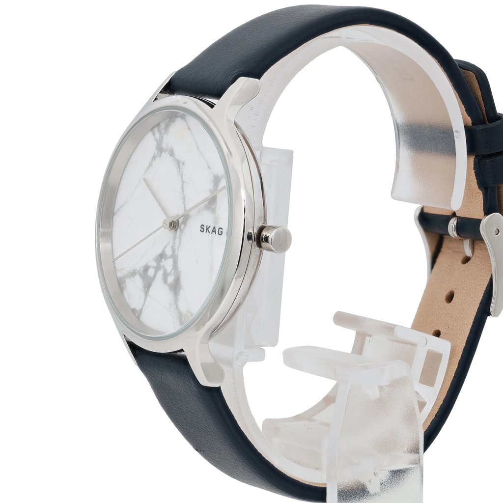 An image of a women's Skagen wristwatch displayed at a slight angle, focusing on the side and front. The watch features a marbled white face with minimalist design elements and a silver-toned case. It is positioned upright on a clear stand, showcasing a dark leather strap. The distance of the shot provides a detailed view of the watch's face and band.