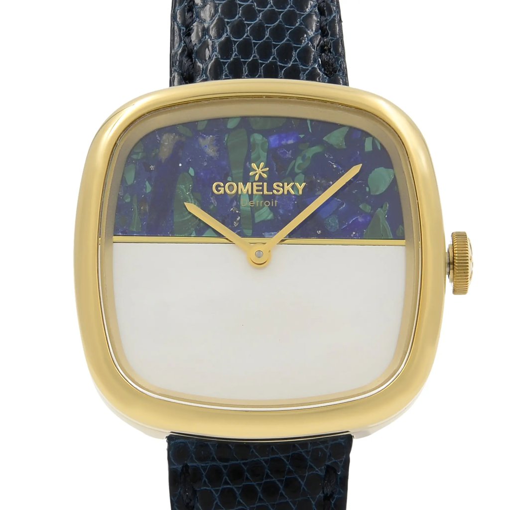 An image of a wristwatch taken from a front close-up angle, showcasing the watch face prominently. The watch features a gold-colored case with a unique dial design, half adorned with a blue and green pattern and the other half in solid white. The brand name "GOMELSKY" and "Detroit" are visible on the patterned section. The watch is unworn, with a textured black strap attached. The crown is positioned on the right side of the case.