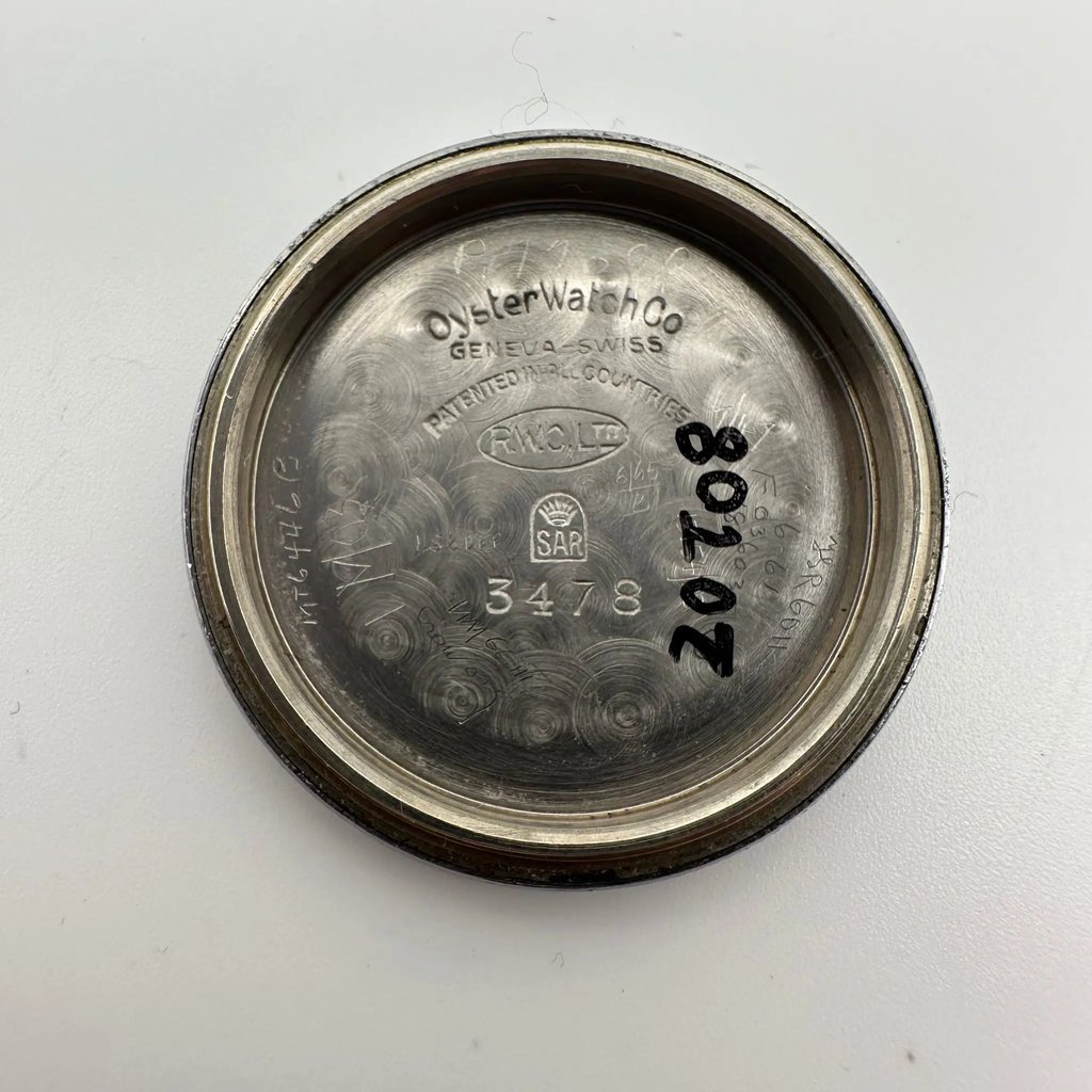 An image of the interior case back of a pre-owned Rolex women's wristwatch. The photograph is taken from a top-down angle, showing the inscriptions and serial numbers inside the circular metal case back. The surface displays engraved text and some hand-written numbers, with a slightly brushed texture. The image is captured at a close distance, highlighting the details of the inscriptions. The background is a plain, light surface.