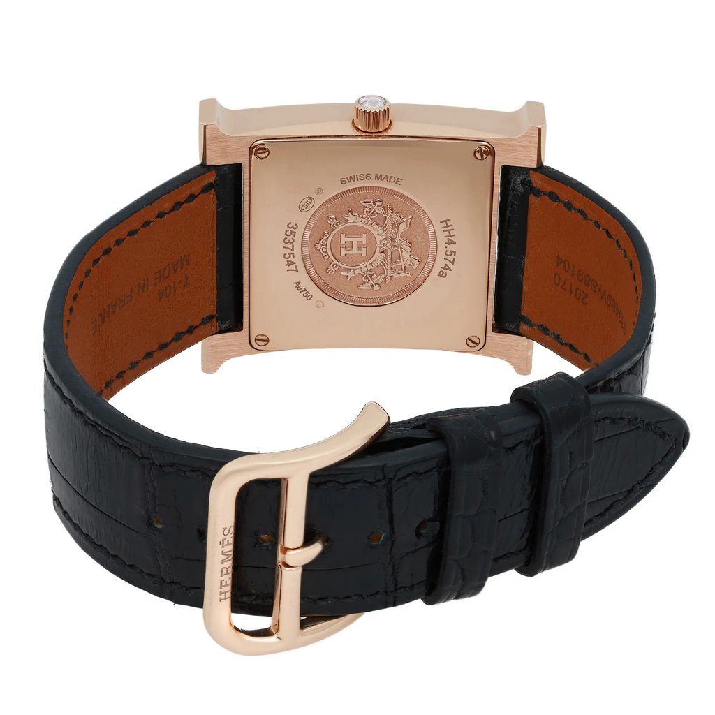 An image of a pre-owned Hermès women's wristwatch viewed from the back. The watch has a square, rose gold case with intricate engravings on the back. The black leather strap is visible, with a matching rose gold buckle prominently displaying the Hermès logo. The watch is positioned at a slight angle, providing a clear view of the details, and the photograph is taken from a close distance.