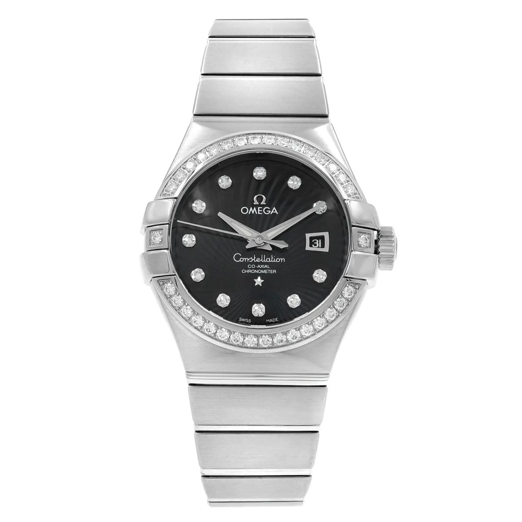 An image of an OMEGA Constellation women's wristwatch displayed from a front-facing angle at a close distance. The watch features an 18k white gold band and a black dial with diamond hour markers. It includes a date indicator and luminous hands, and the bezel is adorned with diamonds. The overall condition appears to be a display model.