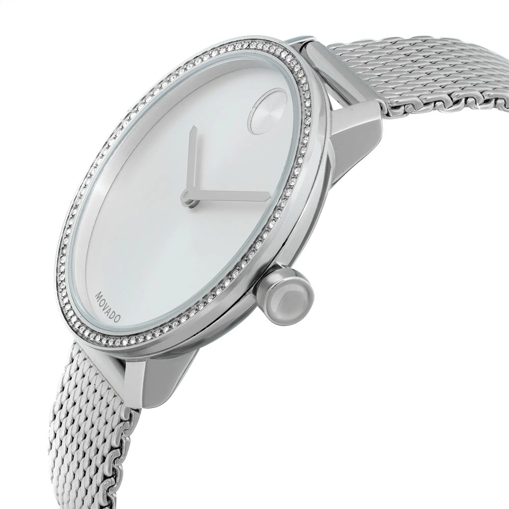 An image of a pre-owned wristwatch captured from a side profile view, showcasing the crown prominently. The watch features a sleek, minimalist design with a silver mesh band. The angle highlights the watch face and the elegant detailing around the bezel, giving a clear view of its refined craftsmanship. The photo is taken at a close distance, emphasizing the watch's intricate features.