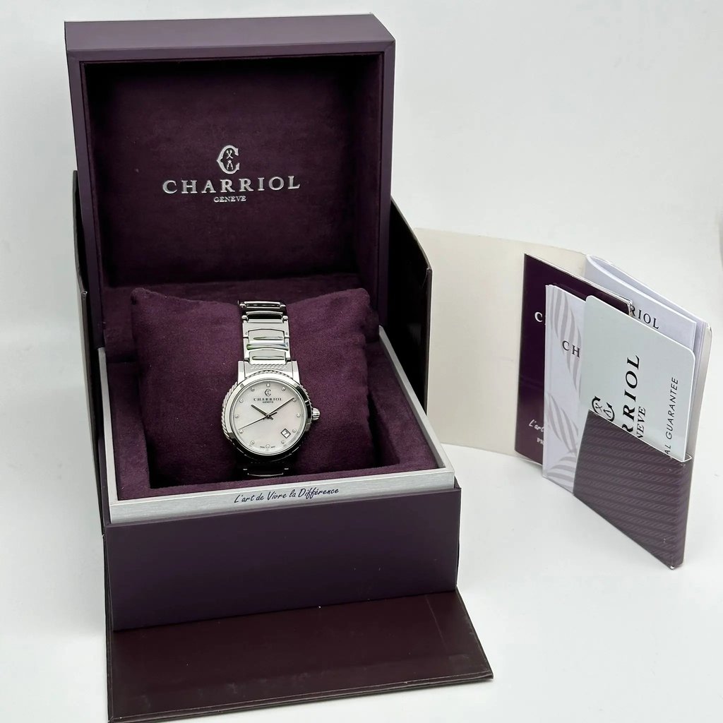 An image of a wristwatch displayed in an open box, viewed from a slightly elevated angle. The box is positioned centrally and contains the unworn watch resting on a plush cushion. The watch features a metal band and a round face. To the right of the box, there are accompanying documents partially visible. The overall setup provides a clear, full view of the product, showcasing its brand and pristine condition.