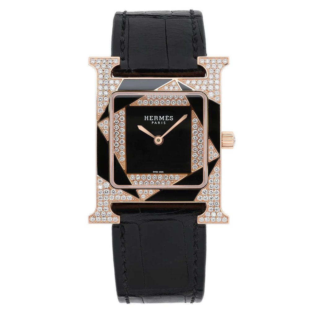 An image of a pre-owned Hermès Heure H Perspective women's 18k rose gold diamond quartz wristwatch, positioned vertically and captured from a front-facing angle. The watch features a black square dial with rose gold hands and is encased in a uniquely designed frame adorned with sparkling stones. The black leather strap is visible, highlighting the luxurious and elegant design of the timepiece.