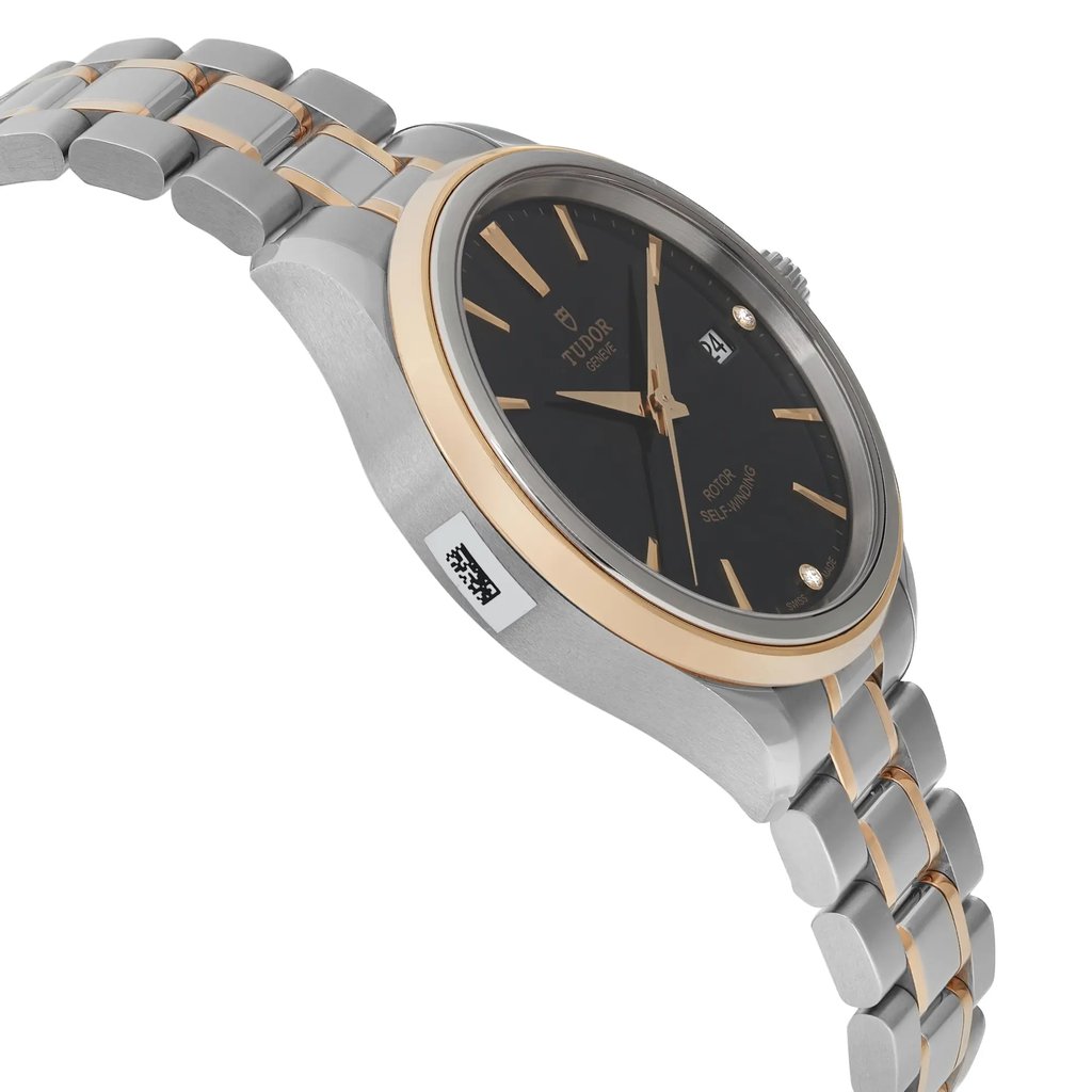 An image of a wristwatch in an unworn condition, captured from a side profile view opposite the crown. The watch features a sleek metal case with a two-tone band, blending silver and gold elements. The angle highlights the smooth contours of the case and the bracelet's links, with the face of the watch partially visible, showing a dark dial. The photograph is taken from a close distance, showcasing the watch's elegant design and craftsmanship.