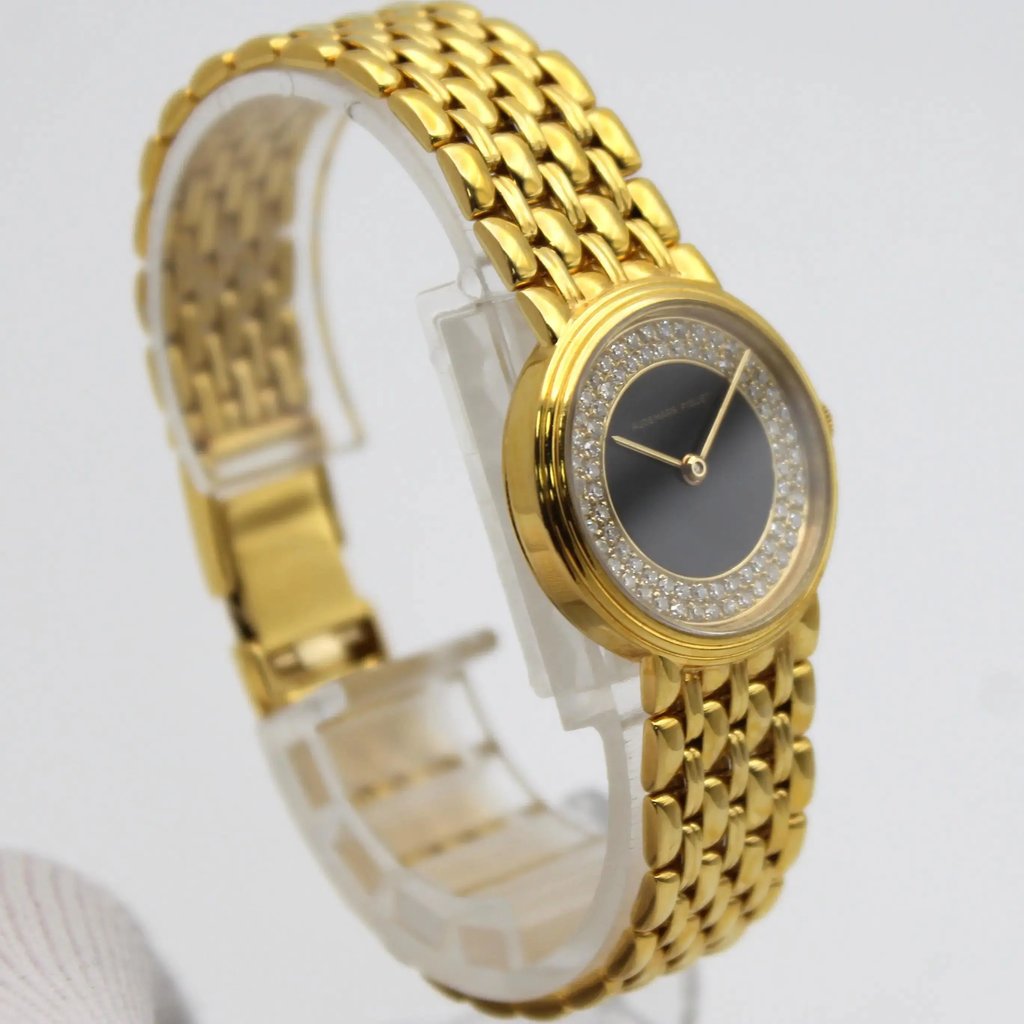 An image of a pre-owned Audemars Piguet women's wristwatch. The watch is positioned at a slight angle, showcasing its elegant design. It features a yellow gold bracelet with a polished, woven pattern. The round watch face has a onyx dial surrounded by a sparkling bezel with diamonds embellishments. The watch is displayed on a transparent stand, captured from a close distance, highlighting its luxurious details.