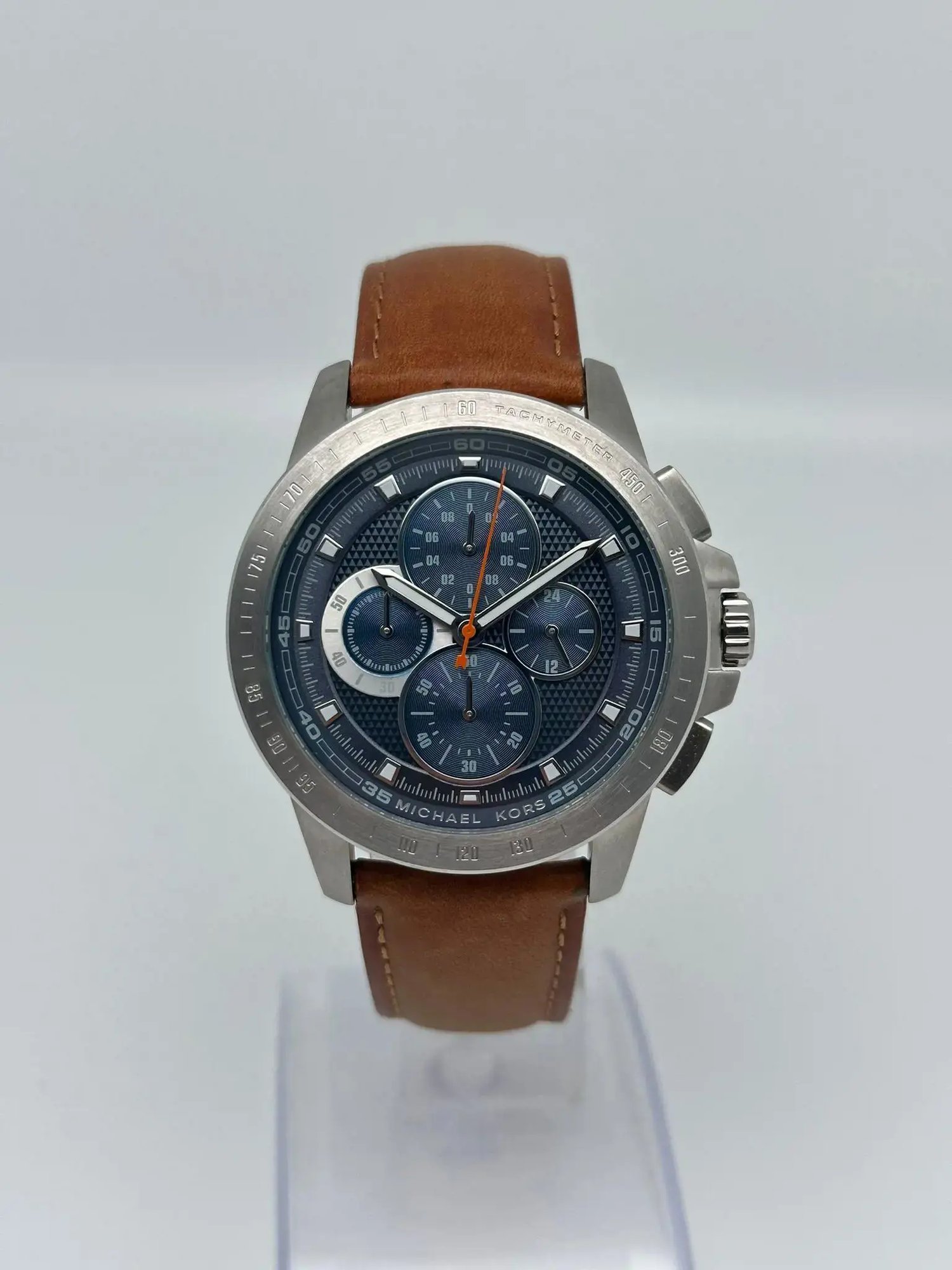 An image of a Wristwatch by Michael Kors. This Pre Owned item is designed for Men, featuring a Casual style. It has a Quartz movement and an Analog display with a Blue dial color. The indices include 12-Hour Dial,Multi Dial,Non-Numeric Hour Marks,Seconds Hand. The band is made of Leather and the case is made of Stainless Steel. The watch has a Round shape with a case size of 43 mm and a case thickness of 11 mm.