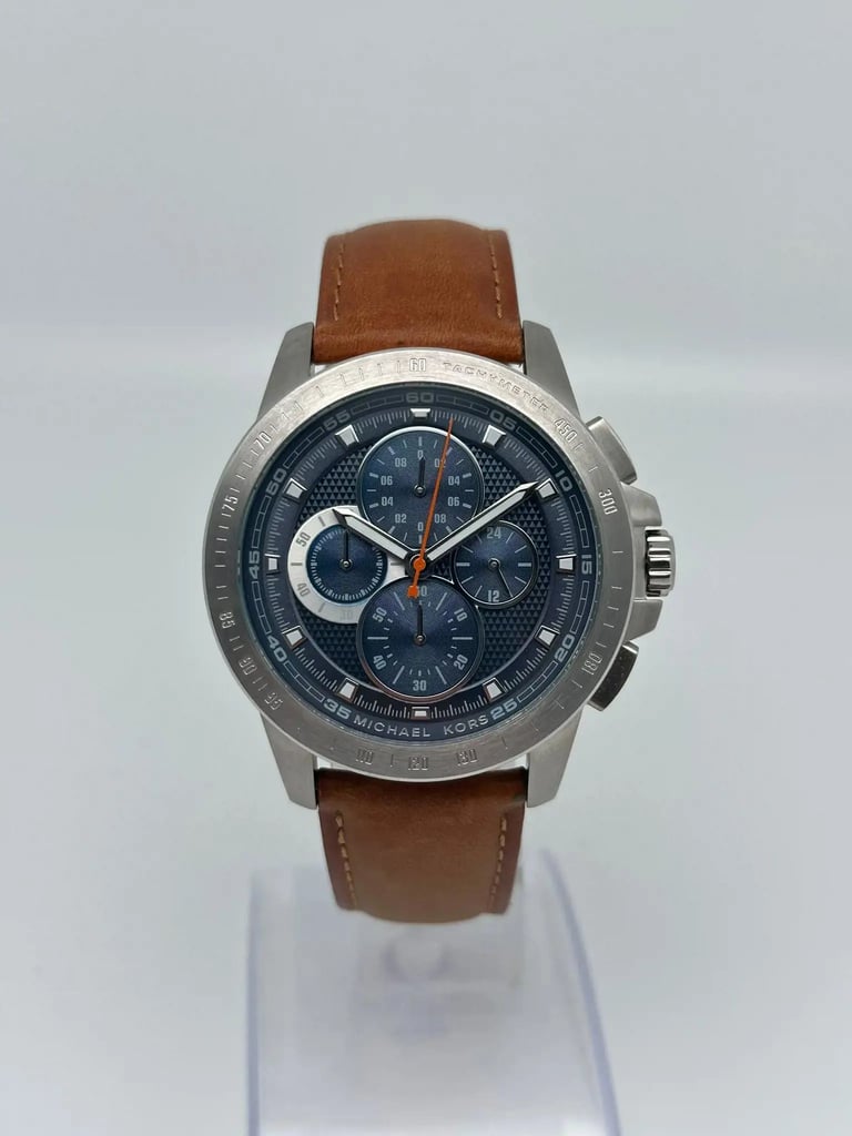 An image of a Wristwatch by Michael Kors. This Pre Owned item is designed for Men, featuring a Casual style. It has a Quartz movement and an Analog display with a Blue dial color. The indices include 12-Hour Dial,Multi Dial,Non-Numeric Hour Marks,Seconds Hand. The band is made of Leather and the case is made of Stainless Steel. The watch has a Round shape with a case size of 43 mm and a case thickness of 11 mm.
