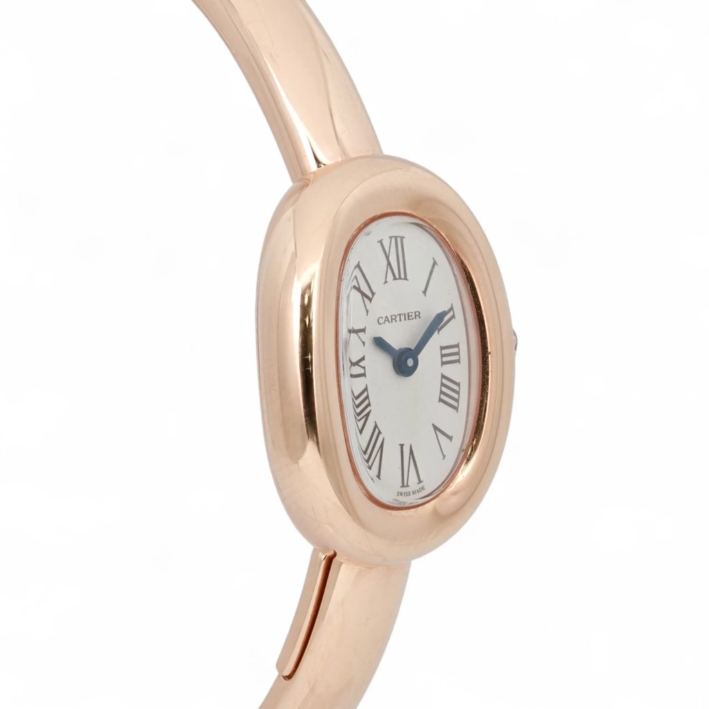 An image of a pre-owned Cartier women's wristwatch. The watch is positioned at a slight angle, showcasing its elegant oval face with Roman numerals on a silver dial. The case and bangle-style bracelet are made of a polished rose gold metal with the shot taken from a close distance to highlight the details. The hands of the watch are blue, adding a subtle contrast to the overall design.