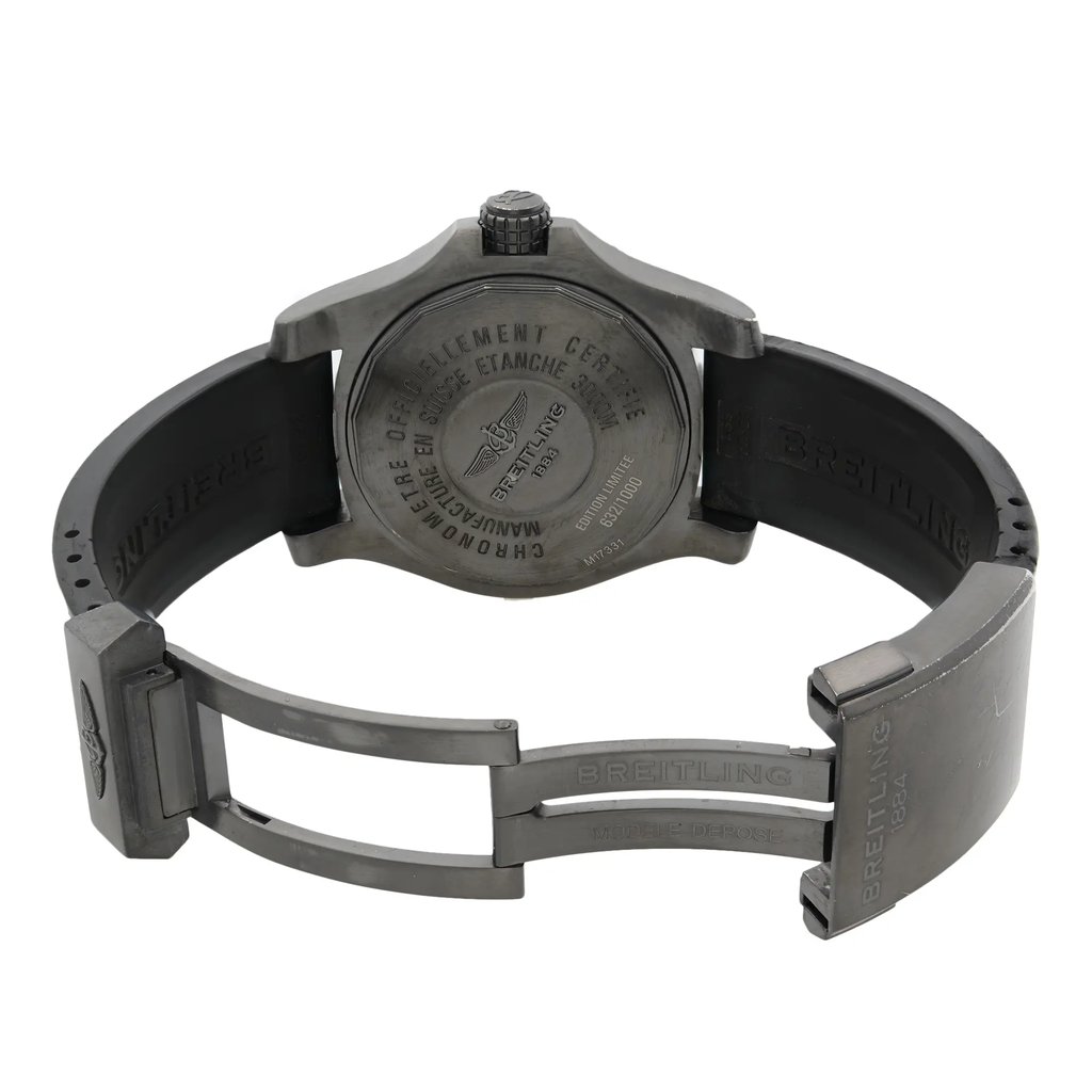 An image of a pre-owned Breitling men's wristwatch with an open clasp, viewed from the back. The watch is positioned at a slight angle with the caseback facing upwards, showing the engraved details. The watch has a round stainless steel case and a screwback caseback. The rubber band displays minor wear and visible scuffs, particularly on the edges of the lugs and case. The clasp is partially extended to the right, and the bezel has some visible scuffs. The distance is close enough to clearly see the text and details on the caseback and clasp.