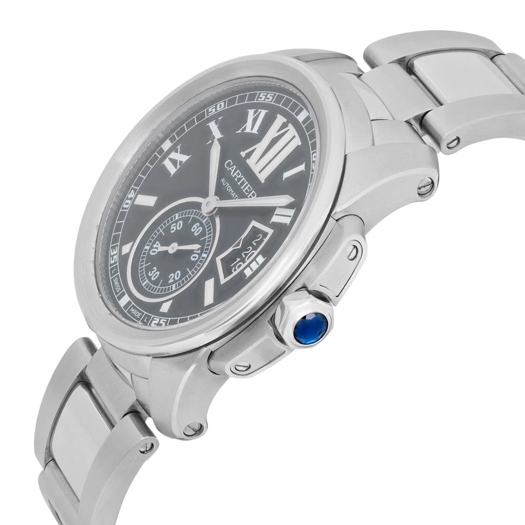 An image of a pre-owned Cartier men's wristwatch taken from a slightly elevated angle, showcasing the right side of the watch. The watch features a silver metal band and case, with a black dial displaying Roman numerals, a date indicator, and luminous hands. The crown is adorned with a blue gemstone. The watch face is in focus, highlighting its elegant design and details.