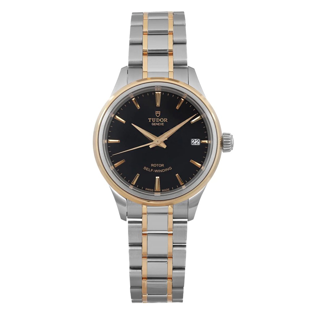 An image of a Tudor Style 28 ladies wristwatch, unworn, captured from a straight-on angle at a close distance. The watch features a black dial with gold hour markers and hands, a date indicator at the three o'clock position, and a two-tone stainless steel and gold bracelet. The crown is visible on the right side of the case.