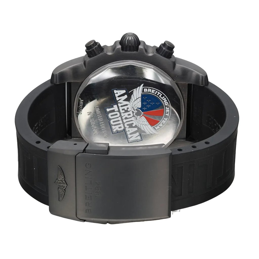 An image of a pre-owned Breitling men's wristwatch with a stainless steel case and a solid caseback featuring an embossed American Tour logo. The watch is displayed at a slight angle with the back view facing upward, showcasing the round shape and the rubber band material. The fold-over clasp with double push-button is in a closed position, and the band loops to the left side of the frame, indicating the watch's flexible strap. The watch is presented in close proximity, offering a clear view of the details on the caseback and the texture of the rubber strap. The watch is pre-owned and may have light signs of wear or scratches. 