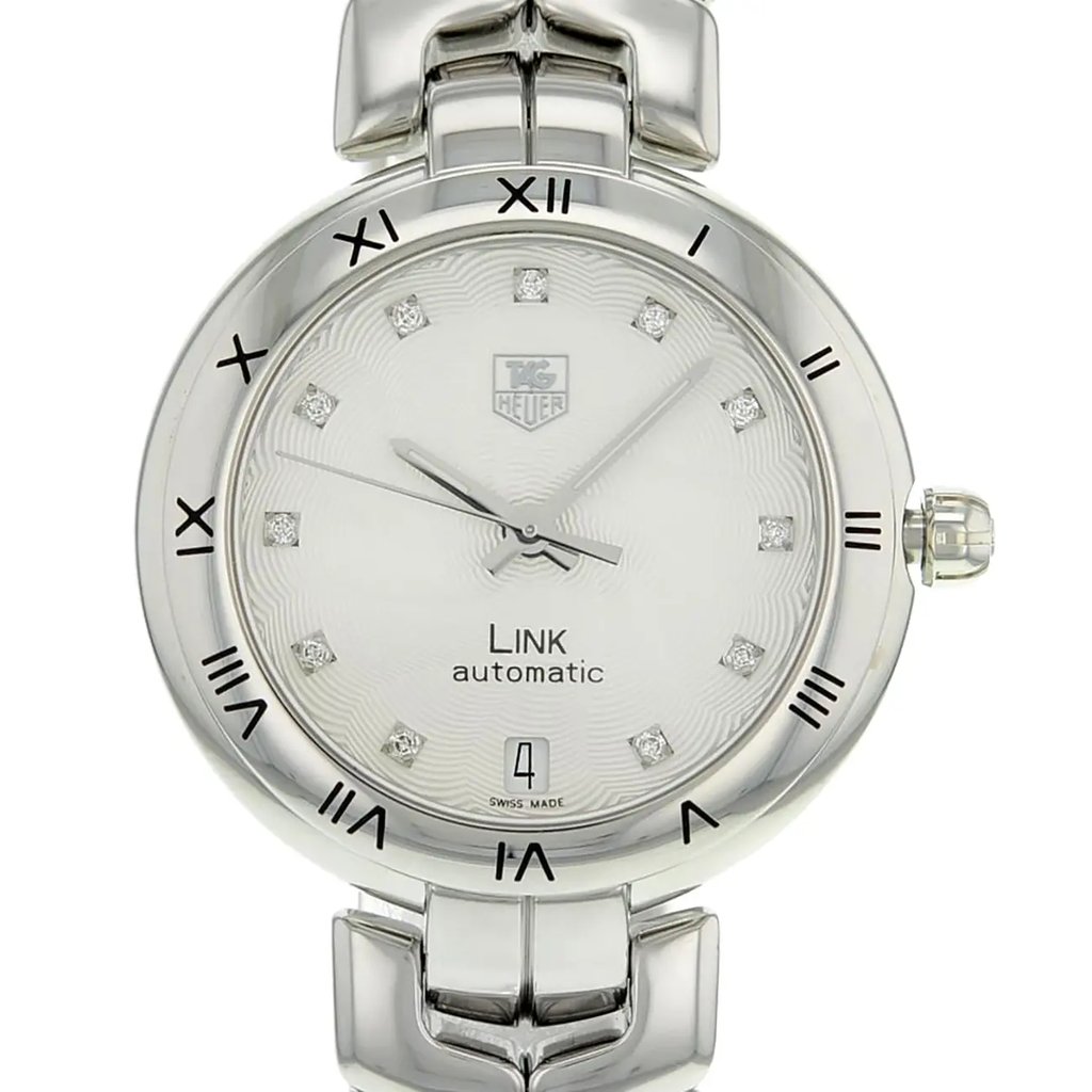 An image of a pre-owned TAG Heuer women's wristwatch, captured from a front close-up angle focusing on the watch face. The round dial is silver with a guilloche pattern and features diamond markers for the 12-hour indices and a date indicator at the 6 o'clock position. The bezel is gray, complementing the stainless steel band and case. The watch is in good condition, suitable for dress or formal occasions.
