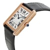 An image of a pre-owned Cartier women's luxury wristwatch with a side profile view showcasing the crown. The watch features a rectangle-shaped case and bezel in rose gold with minor signs of wear, complemented by a silver dial. The black leather band attaches to the sides of the rose gold case. The crown is adorned with a blue cabochon stone. The watch is photographed from a close distance at a slight angle to emphasize the side profile and crown details.