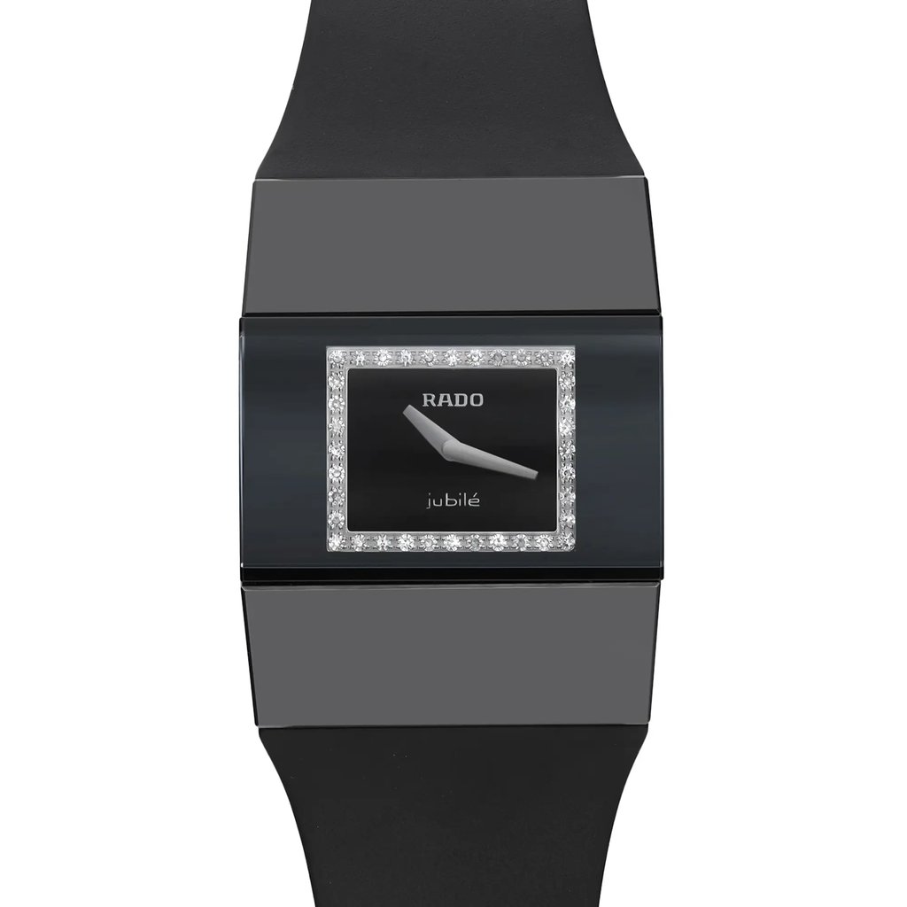 An image of a new Rado women's wristwatch with visible micro scratches on the case, viewed from a close-up front angle showing the watch face. The watch features a casual style with a rectangular ceramic case and a black rubber band. The dial is black with a diamond pattern and is framed by a black bezel, adorned with diamonds. The dial has no hour marks, instead having the Rado logo and the word "jubilé" underneath. The condition is classified as excellent, despite the minor defects from store handling.