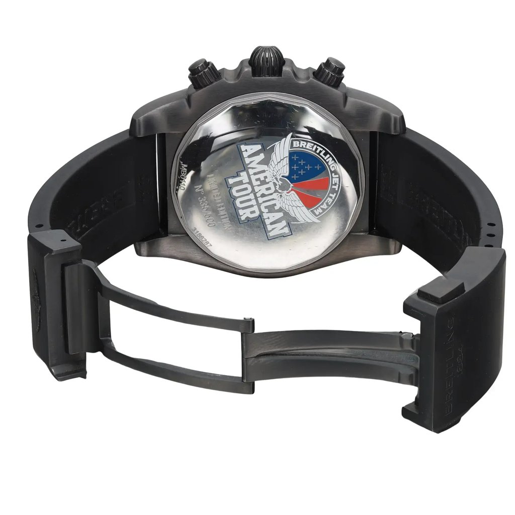 An image of a pre-owned Breitling men's wristwatch with a round stainless steel case and solid caseback featuring an "American Tour" engraving. The watch is presented from a rear view, showcasing its open fold-over clasp with double push-button on a black rubber band. The watch is angled to display the clasp mechanism partially extended on the right side, and it is photographed at a close distance, ensuring clear visibility of the details on the caseback. The watch is pre-owned and may show light signs of wear and scratches. 