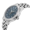 An image of a pre-owned men's Patek Philippe wristwatch, viewed from a slightly elevated angle and positioned to the right. The watch features a white gold bracelet and a blue dial with a date indicator and moon phase display. The crown is visible on the side, and the watch is shown in close-up detail.