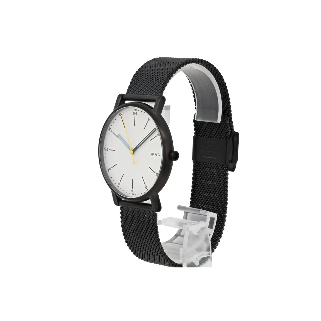 An image of a Skagen women's wristwatch displayed at a slight angle. The watch features a minimalist white dial with slender black hour markers and a yellow second hand. It has a black mesh strap and is positioned upright on a clear stand, allowing a clear side view of its sleek design. The photo is taken from a close distance, highlighting the watch's elegant and modern style.