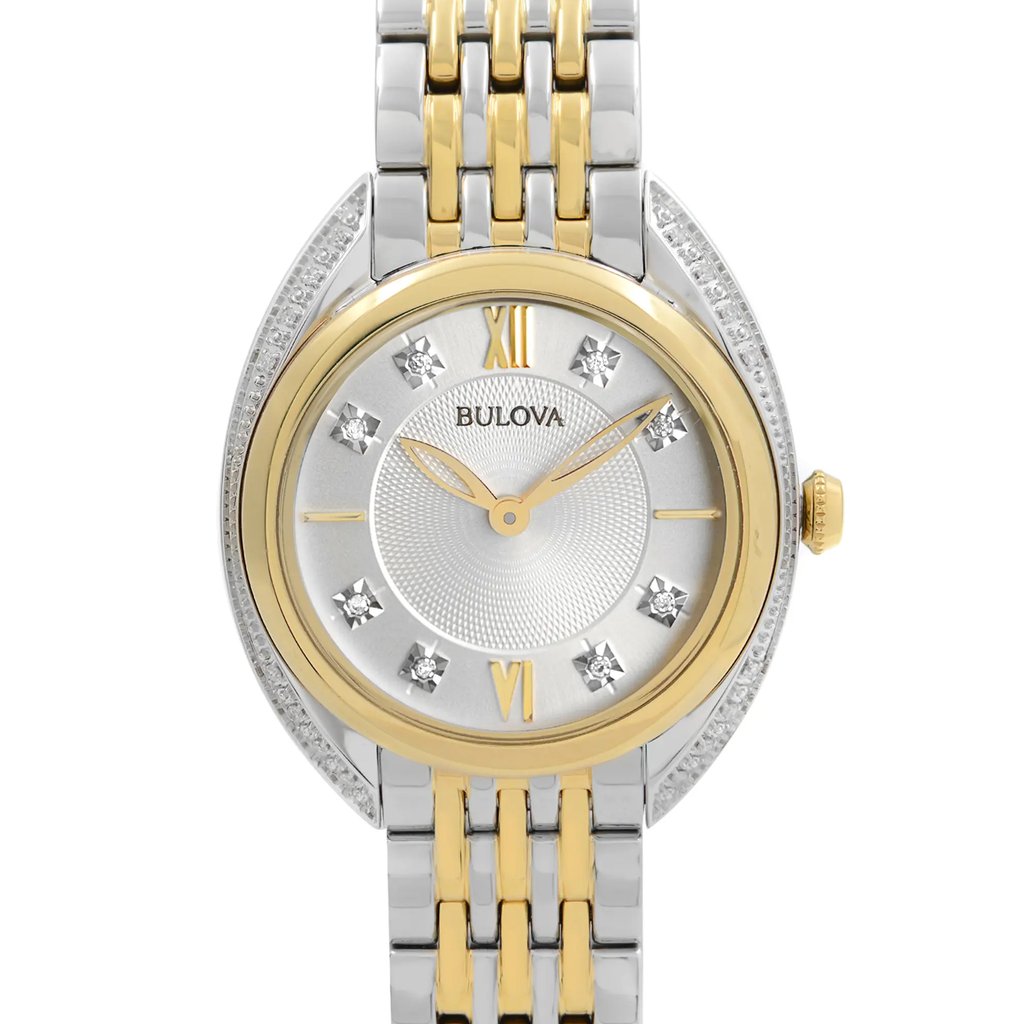 An image of a Bulova women's wristwatch in excellent condition, taken from a frontal close-up angle showcasing the watch face. The watch features a round silver dial with diamond markers at the 3, 6, 9, and 12 positions, complemented by stick indexes and Roman numerals. The yellow gold-tone bezel is encrusted with crystals and the band is made of two-tone stainless steel. The Bulova logo is visible at the top of the dial, and the hands are positioned at ten past ten. The crown is on the right side of the case. The watch appears as a display model with a clear view of the dial and upper part of the bracelet, with the background and lower part of the bracelet fading out of focus.