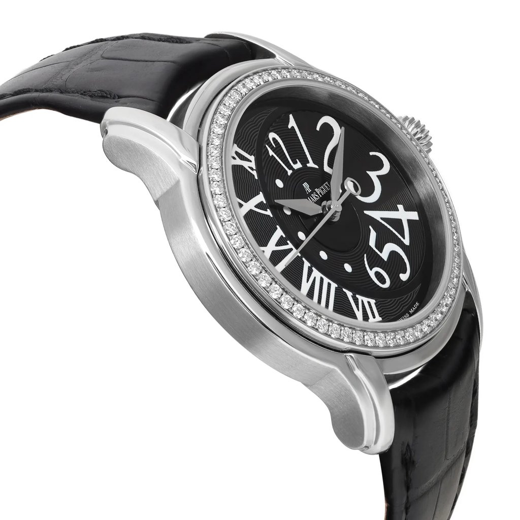 An image of a pre-owned wristwatch captured from a side profile view, opposite the crown. The watch features a silver-toned case with a diamond-studded bezel and a black strap. The angle highlights the intricate design of the black dial with large, stylized white numerals. The photo is taken at a close distance to emphasize the watch's details and craftsmanship.