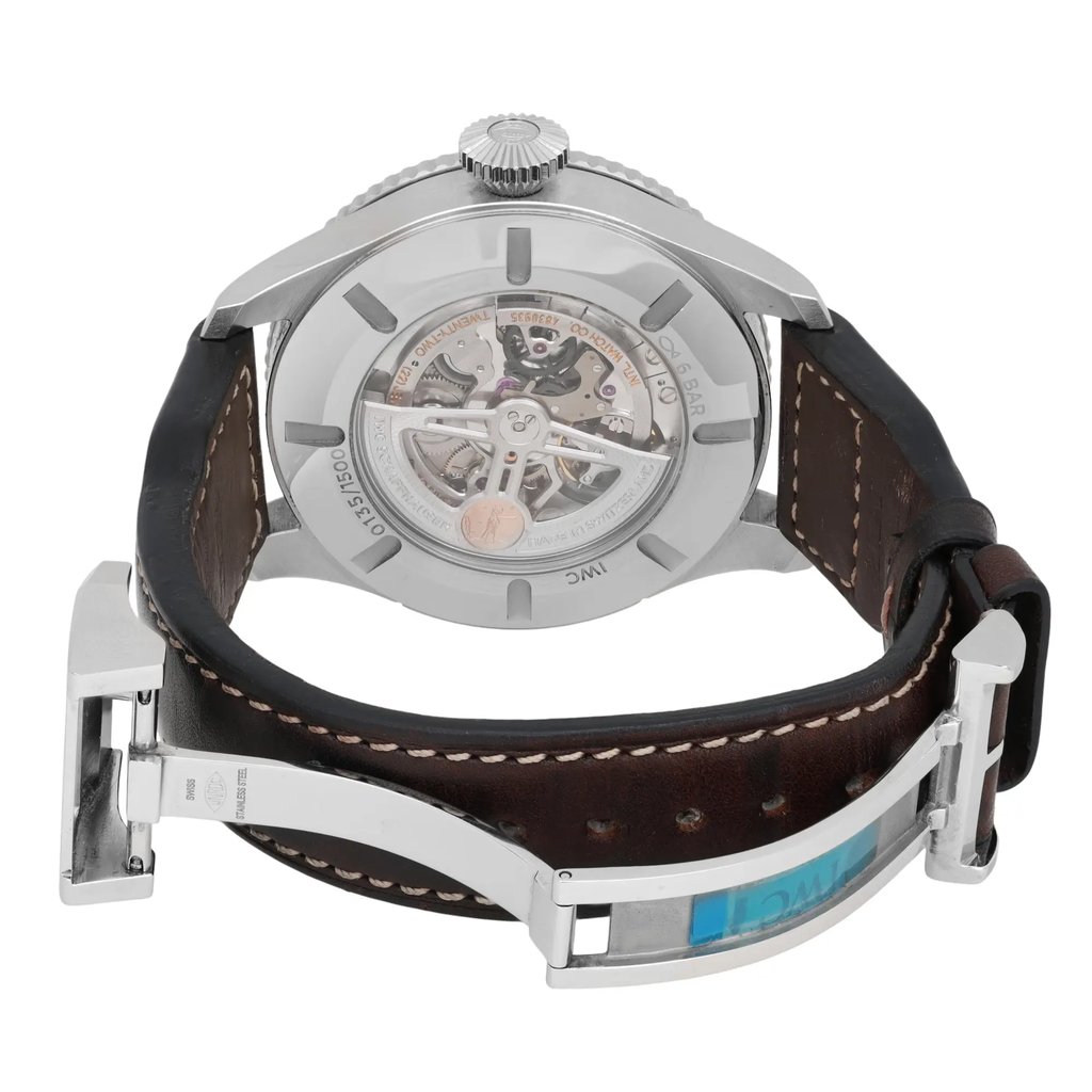 An image of a pre-owned IWC Timezoner Le Petit Prince Edition men's wristwatch. The watch is shown from the back at a slight angle, highlighting the intricate mechanisms visible through the transparent case back. The stainless steel case is paired with a dark brown leather strap featuring white stitching. The watch is positioned to showcase its clasp and the luminous hands feature, with the image taken from a close distance.