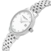 An image of an unworn RAYMOND WEIL women's wristwatch in a dress/formal style. It presents a side profile view with the crown visible, positioned at a slight angle to show off the stainless steel band and case. The watch has a round shape with a white mother of pearl dial featuring diamond hour markers and the RAYMOND WEIL logo. A date window is visible at the 3 o'clock position. The image is taken from a close distance, emphasizing the details and design of the watch.