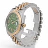 An image of a pre-owned unisex Rolex wristwatch positioned at a slight angle. The watch features a green dial with luminous hands, a date indicator, and a two-tone metal bracelet. The photo is taken from a close distance, showcasing the gold bezel and the brand logo on the crown.