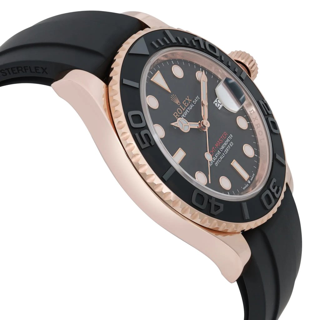An image of a pre-owned men's Rolex wristwatch, captured from a close-up side angle. The watch features a rose gold case and a black bezel with engraved numerals. The black dial includes luminous hands and a date indicator. The watch is positioned with the crown on the right side, and the rubber strap is visible in the foreground.