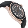 An image of a pre-owned men's Rolex wristwatch, captured from a close-up side angle. The watch features a rose gold case and a black bezel with engraved numerals. The black dial includes luminous hands and a date indicator. The watch is positioned with the crown on the right side, and the rubber strap is visible in the foreground.