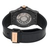 An image of a pre-owned men's Hublot wristwatch. The watch is positioned with the back facing the viewer, showcasing its intricate mechanical movement through a transparent case back. The angle is slightly elevated, providing a clear view of the watch's inner workings and branding. The distance is close, emphasizing details such as the gold-tone crown and clasp, as well as the black strap with a textured pattern.
