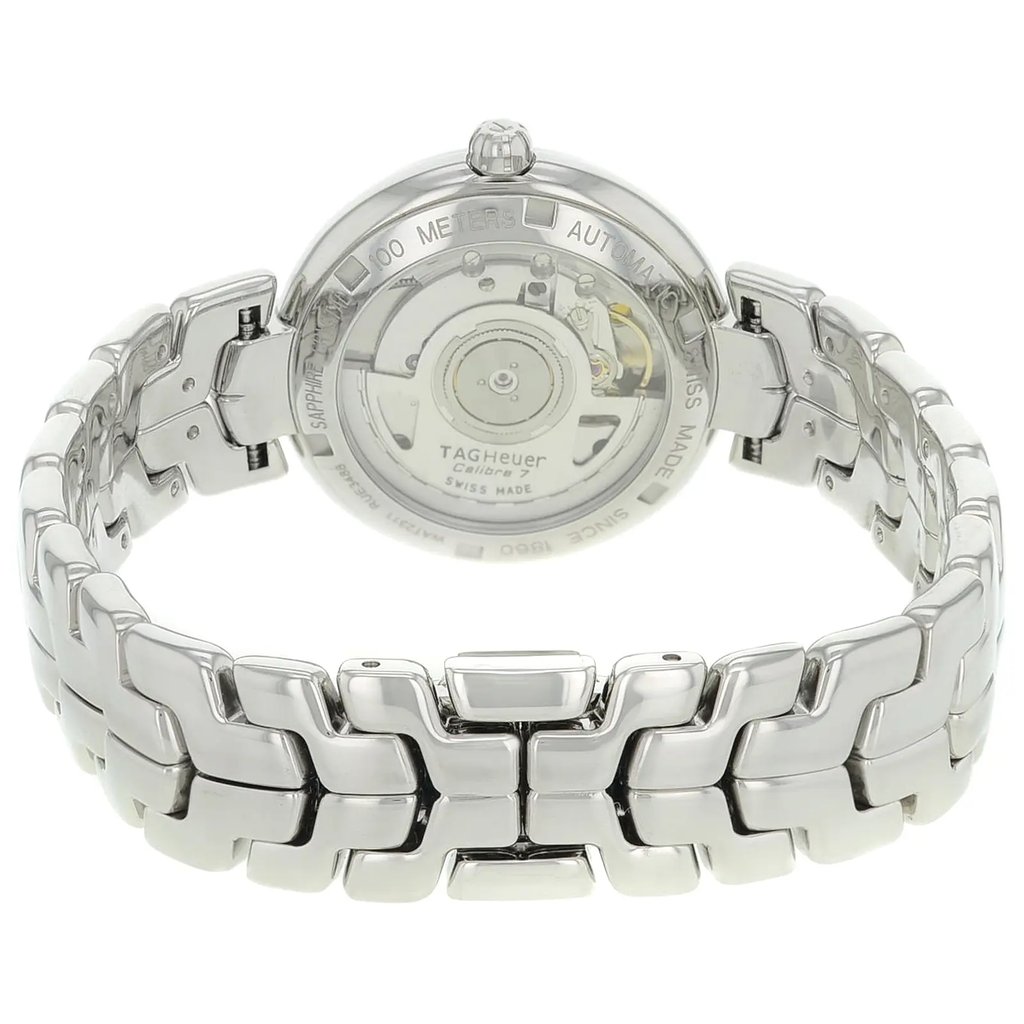 An image of a pre-owned TAG Heuer women's wristwatch viewed from the back, showcasing the exhibition caseback with visible internal mechanisms. The watch has a round stainless steel case and band. It features a double-locking fold-over clasp, prominently displayed in a close-up, angled view. The stainless steel links and the intricacies of the clasp are clearly visible, emphasizing the watch's craftsmanship.