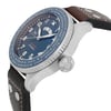 An image of a pre-owned men's IWC Timezoner Le Petit Prince Edition wristwatch taken from a side angle at close range. The watch features a blue dial with luminous hands and bold white numerals. The bezel displays various city names, and the watch has a textured crown. The brown leather strap with rivet details is partially visible.