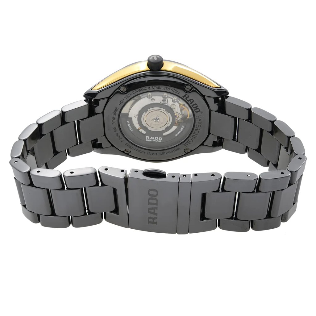 An image of a pre-owned wristwatch viewed from the back, showcasing the watch's open clasp. The angle is slightly elevated, providing a clear view of the intricate details on the back of the watch case and bracelet. The focus is close, highlighting the brand name engraved on the clasp and the visible mechanical components through the transparent case back.