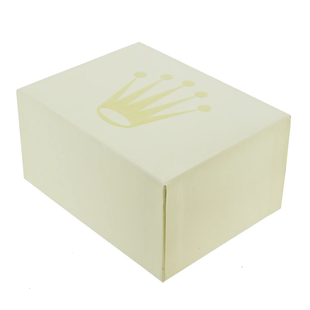 An image of a wristwatch box viewed from a slightly elevated angle, showcasing its full rectangular form. The box is positioned centrally against a plain background, and features a prominent gold crown logo on the top surface. The image captures the box at a close distance, highlighting its simple, elegant design.