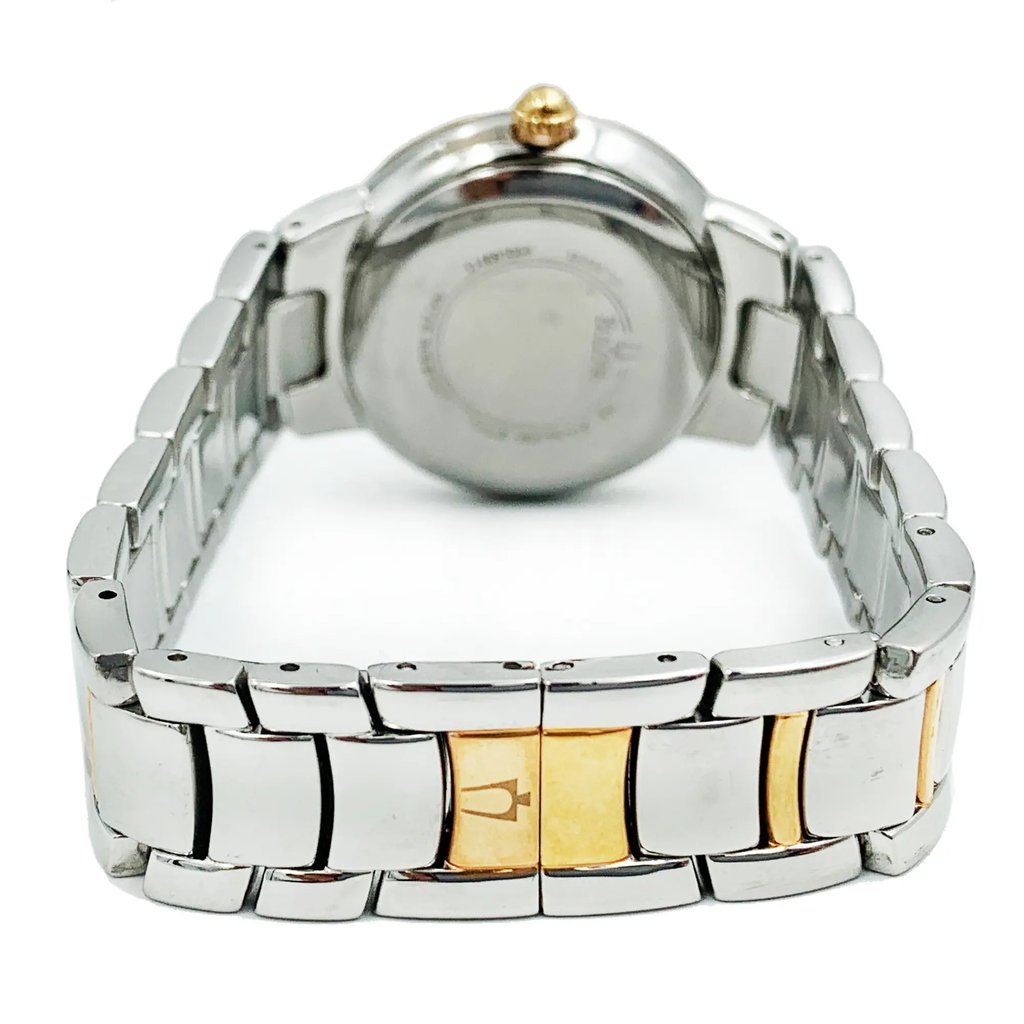 An image of a pre-owned Bulova women's wristwatch, showcasing the back view. The watch features a stainless steel case with a snap caseback, visible at the center with brand engravings. Attached is a stainless steel band with a two-tone design, highlighting a butterfly clasp closed at the foreground. The round watch shape is emphasized by the angle, with the watch positioned upright and the camera focused on the clasp, providing a clear view from a close distance.