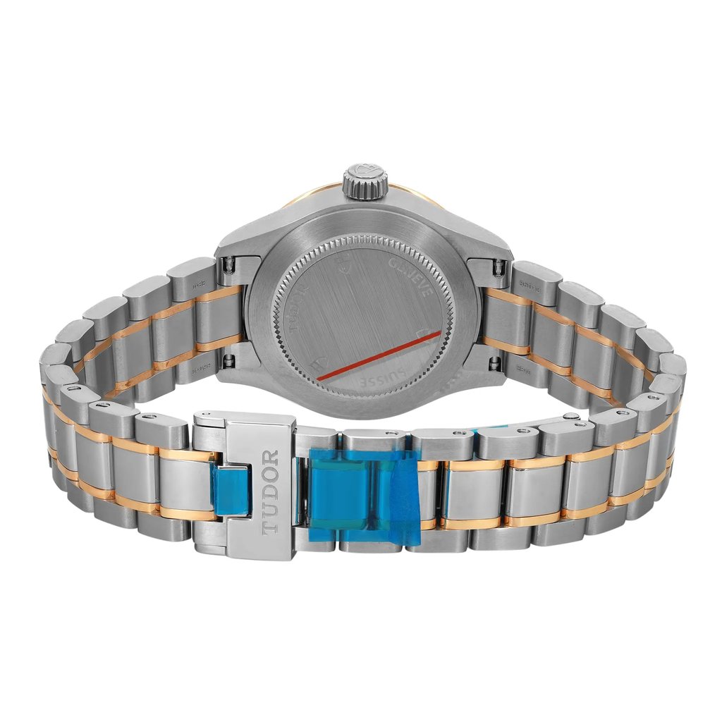 An image of an unworn wristwatch captured from the back view, focusing on the closed clasp. The watch features a stainless steel link band with gold accents. The clasp displays the brand name "Tudor" and is partially covered with a protective blue film. The watch caseback is visible, showcasing a brushed finish. The image is taken from a close distance, emphasizing the details and texture of the watch components.